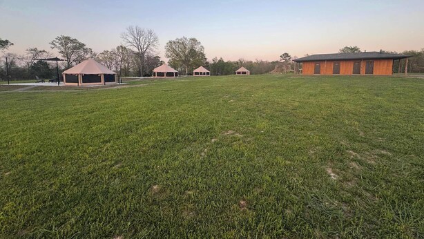 A large grassy field with several small structures, including a pavilion and a building with a sloped roof. - RV site 1 @ The River Bluff Cabins (Tahlequah)