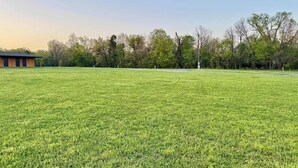A grassy field with a building in the background. - RV Site  4 @ The River Bluff Cabins (Tahlequah)