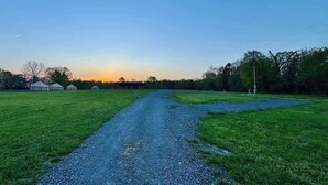 A gravel path leading to a building surrounded by green fields and trees. - RV Site 5 @ The River Bluff Cabins (Tahlequah)