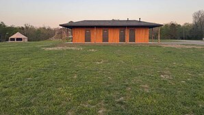 A single-story wooden building with a flat roof, a front door, and two windows on the side. - RV Site 5 @ The River Bluff Cabins (Tahlequah)