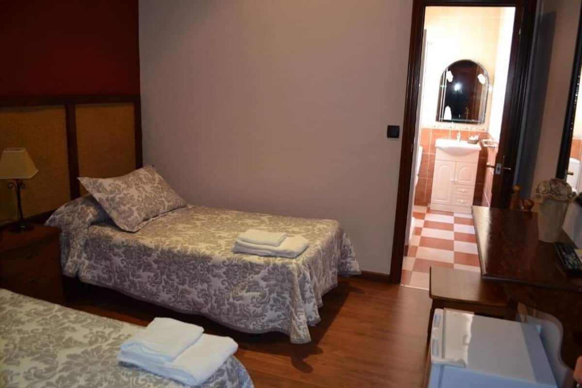 Ένα δωμάτιο ξενοδοχείου με ένα κρεβάτι, ένα γραφείο και ένα μπάνιο, τα οποία φαίνονται μέσα από μια ανοιχτή πόρτα.