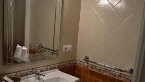 A bathroom with a white sink, a mirror with lights, and a tiled wall. - HOSTAL PENSION LA RUTA (Escacena del Campo)