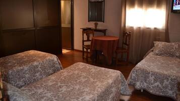 Une chambre avec deux lits, une petite table ronde avec des chaises, un miroir au mur et une fenêtre avec des rideaux.