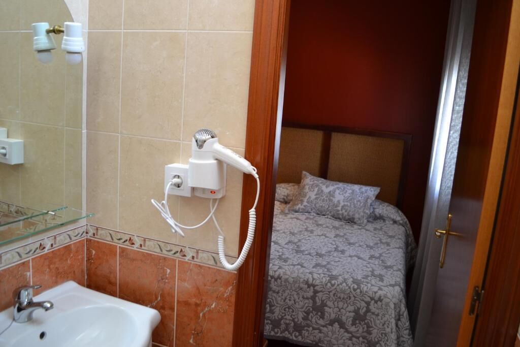 Un baño con lavamanos, espejo y secador de pelo en la pared.