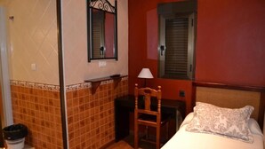 A hotel room with a bed, a chair, a desk, a mirror, and a window with blinds. - HOSTAL PENSION LA RUTA (Escacena del Campo)