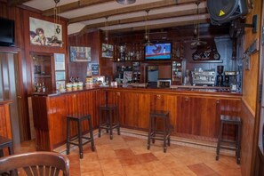 A bar area with wooden bar stools, a television, and various bar equipment. - HOSTAL PENSION LA RUTA (Escacena del Campo)
