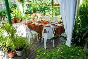 An outdoor dining area with a table set for four, surrounded by potted plants and a green fence. - Beb "Ziu Antoi and Aunt Srivia" (Sestu)