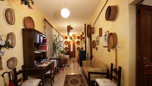 Un salon chaleureux avec un canapé, des fauteuils, une table basse et un coin repas comprenant une table et des chaises. Les murs sont décorés de vases et d’une plante.