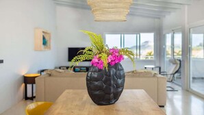 Ett modernt vardagsrum med ett träbord, en svart, strukturerad vas med rosa blommor och en flätad lampa.