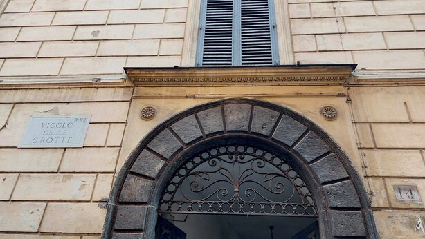 Un ingresso ad arco con una griglia metallica decorativa, un cartello che riporta 'Vicolo delle Grotte' e una finestra con persiane.