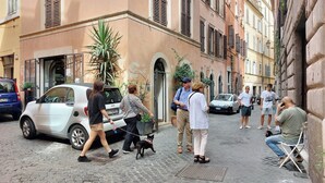 Una strada acciottolata con pedoni, auto parcheggiate e palazzi con portali ad arco.