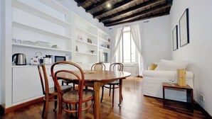 Una cucina moderna con mobili bianchi, sedie di legno e un tavolo da pranzo. Si nota un divano bianco e un piccolo tavolino in legno con un bicchiere.