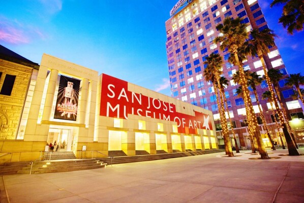 La façade extérieure du musée d’art de San José, avec une enseigne rouge bien visible, une architecture classique et des palmiers au premier plan.