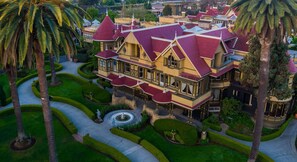 Un grand bâtiment imposant, doté d’un toit rouge et de plusieurs étages, entouré de jardins bien entretenus et de palmiers.
