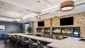 A modern bar area with a long counter, multiple bar stools, and a variety of liquor bottles. - Prime Milpitas Location | Pool, Fitness & Dining (Milpitas)
