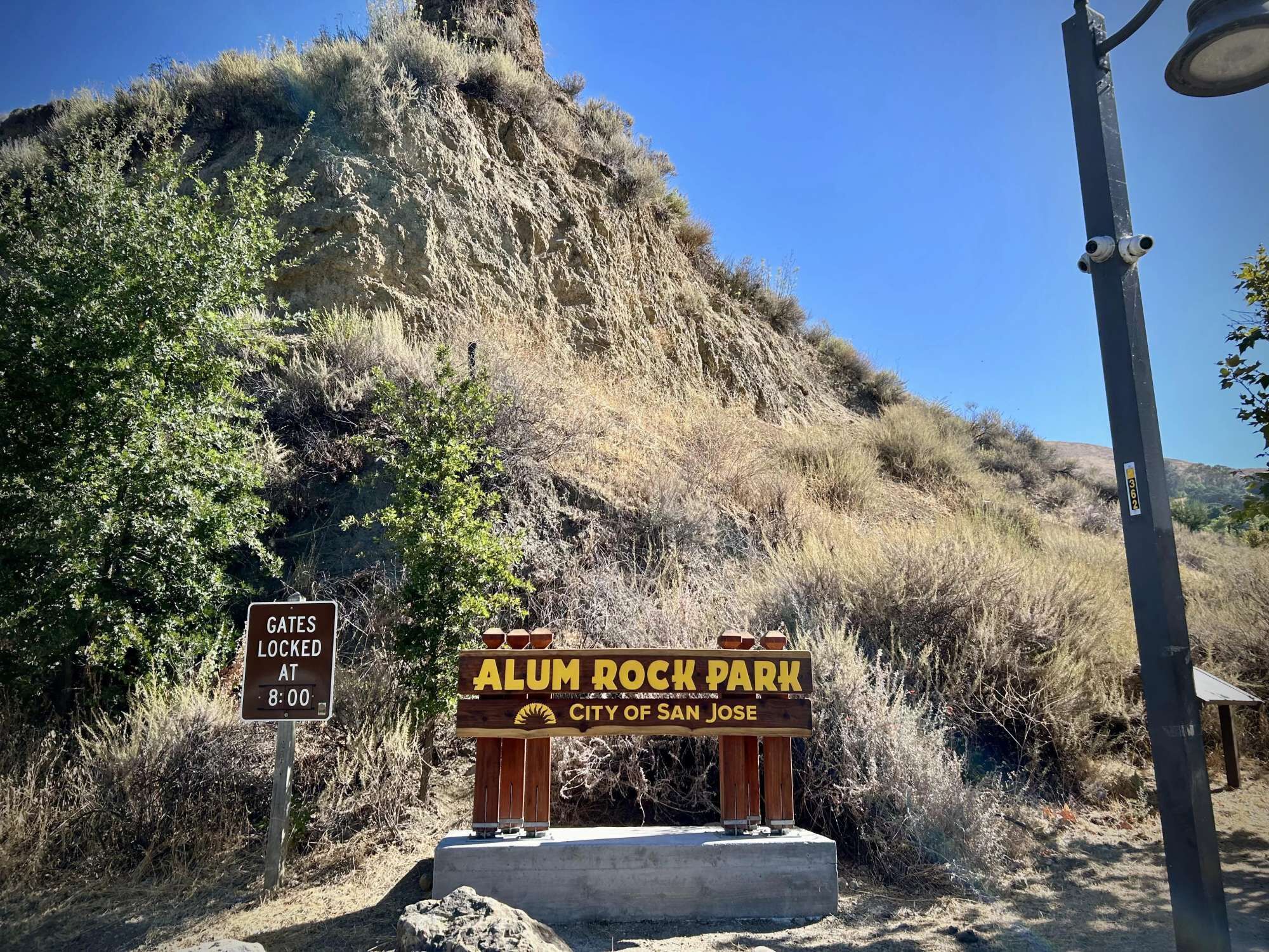 A sign for Alum Rock Park in the City of San Jose, with a gate locked at 8:00 AM.