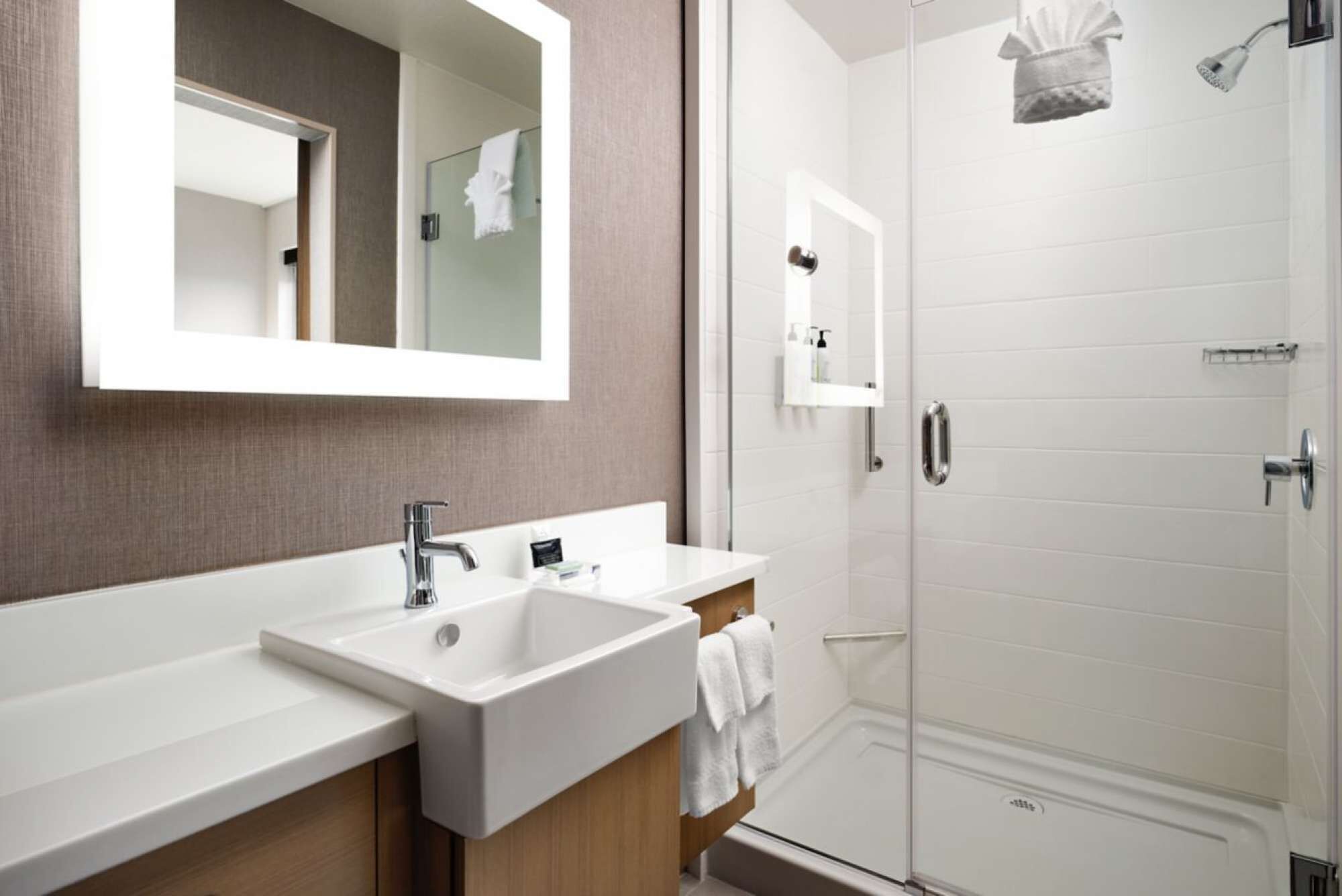 A modern bathroom with a large mirror, two sinks, a shower, and a towel rack.