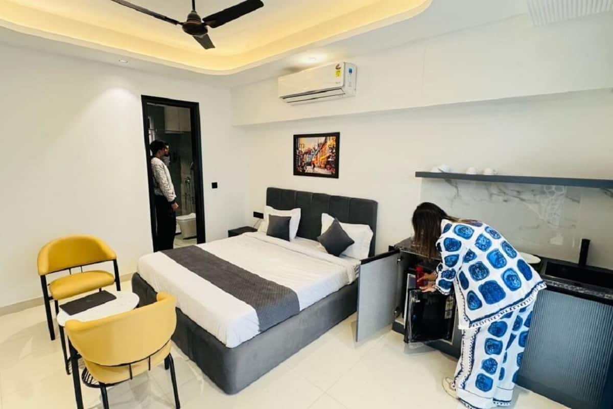 A modern hotel room with a bed, a desk, a chair, and an air conditioning unit.