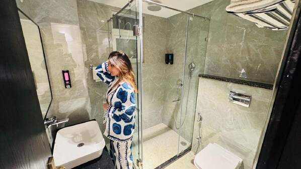 A modern bathroom with a glass-enclosed shower, a white sink, and a toilet. - Reebah Inn & Suites (Gurugram)
