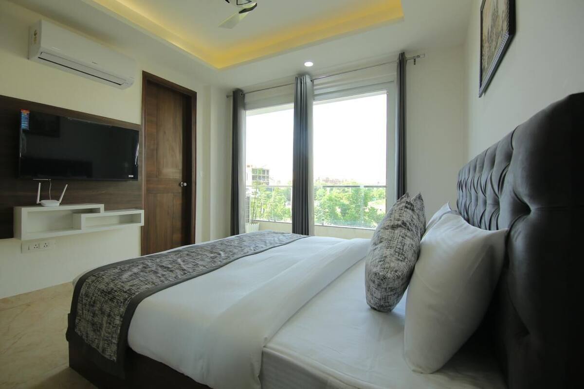 A modern hotel room with a large bed, a flat-screen TV, a balcony with a view, and a ceiling fan.
