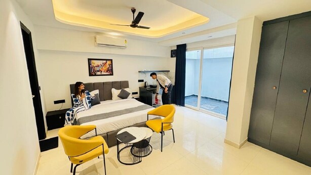 A modern hotel room with a large bed, a desk, and a chair. There is a window with a view of the outside. - Reebah Inn & Suites (Gurugram)
