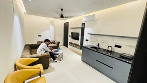 A modern living room with a sofa, a coffee table, and a TV. There is a kitchen area with a countertop and a sink. - Reebah Inn & Suites (Gurugram)