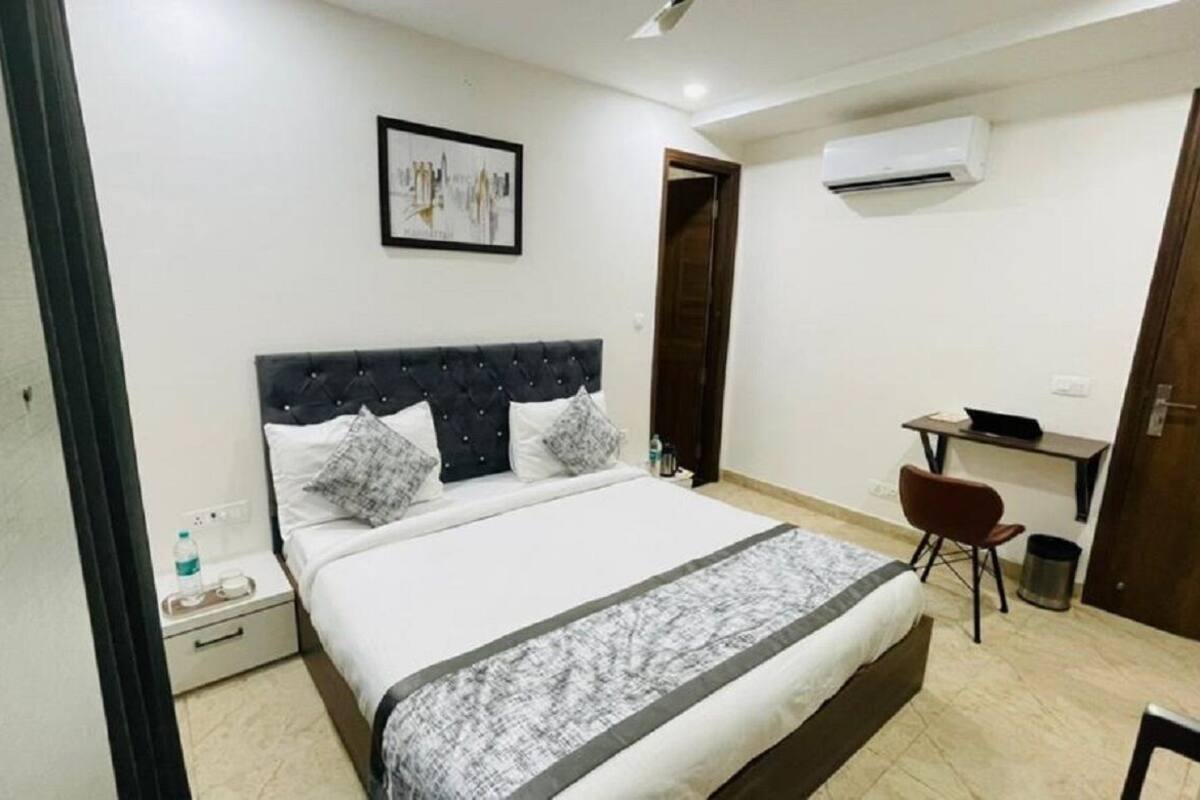 A bedroom with a bed, a desk, a chair, an air conditioner, and a picture on the wall.