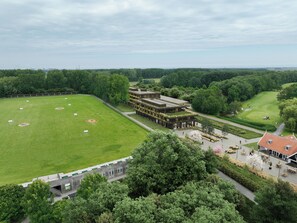 A large green field with a building complex adjacent to it, surrounded by trees. - Spaarnwoude Park Hotel (Velsen-Zuid)