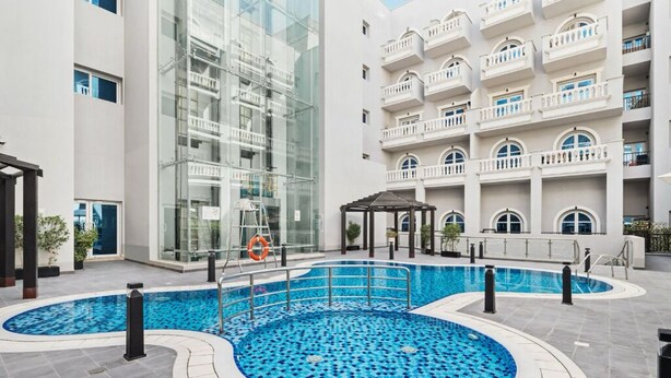 Un hôtel moderne doté d’une piscine centrale, d’une façade en verre et d’un bâtiment à plusieurs étages avec des balcons.