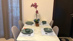 Une table à manger est dressée avec quatre assiettes vertes, deux bols et des couverts. Un pot d’orchidée est posé sur la table.