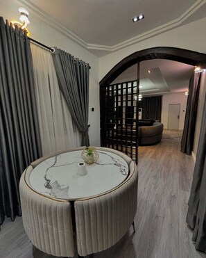 A modern room with a round marble table, grey curtains, and a black partition. - Bigjay Apartment (Abuja)