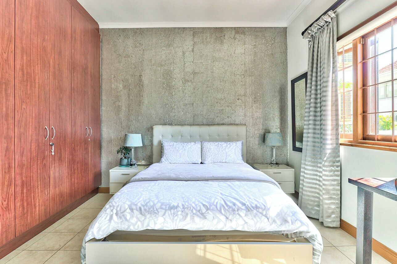 Une chambre à coucher avec un lit, des tables de chevet, une armoire en bois et un mur en béton.
