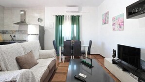 Una sala de estar con un sofá, una mesa de centro, un televisor y un comedor con sillas y una mesa.