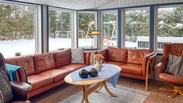 Un salon chaleureux avec un canapé en cuir marron, une table basse en bois et une vue sur un paysage enneigé par de grandes fenêtres.