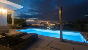 A modern outdoor swimming pool with a city view at dusk.