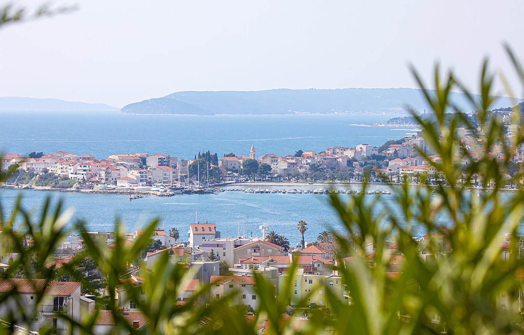 A coastal town with buildings along the waterfront, a clear view of the sea, and hills in the background.