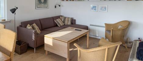 Una sala de estar con un sofá, una mesa de centro de madera, sillas de mimbre y un radiador.