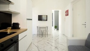 A modern kitchen with a marble floor, a dining area with a table and chairs, and a TV mounted on the wall. - Elmi 1 – Cool apartment with on-site parking  (Arona)