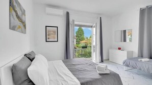 Une chambre moderne avec un lit, une table de chevet, un petit bureau et une vue sur un jardin, visible à travers une porte ouverte.