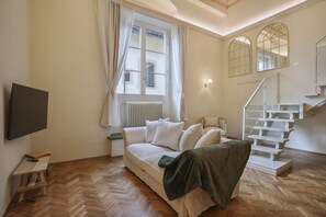 A room with a sofa, a TV, a staircase, and a window with curtains. - Palazzo Galli Tassi Collection - Loft 1 (FIRENZE)