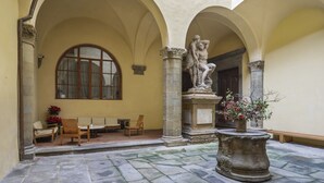 Un patio exterior con suelo de piedra, una estatua y arreglos de asientos.