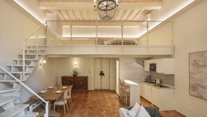 Un interior amplio con piso de madera en serpeto, un comedor con mesa y sillas, una cocina con gabinetes blancos y una escalera que sube a un nivel superior.