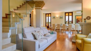 Un salon comprenant un canapé, un fauteuil jaune, un coin repas, un escalier et une cheminée.