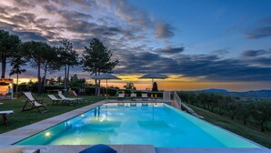 Une piscine entourée d’arbres, avec des chaises longues et des parasols, offrant une vue imprenable sur le coucher du soleil.