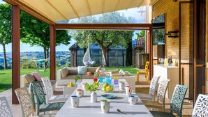 Une terrasse extérieure avec une table dressée pour le repas, entourée de chaises et d’un canapé, offrant une vue sur la campagne.