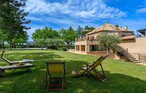 A spacious outdoor area with a well-maintained lawn, outdoor furniture, and a brick building with a tiled roof. - Villa il Tempo Ritrovato (Macerata)