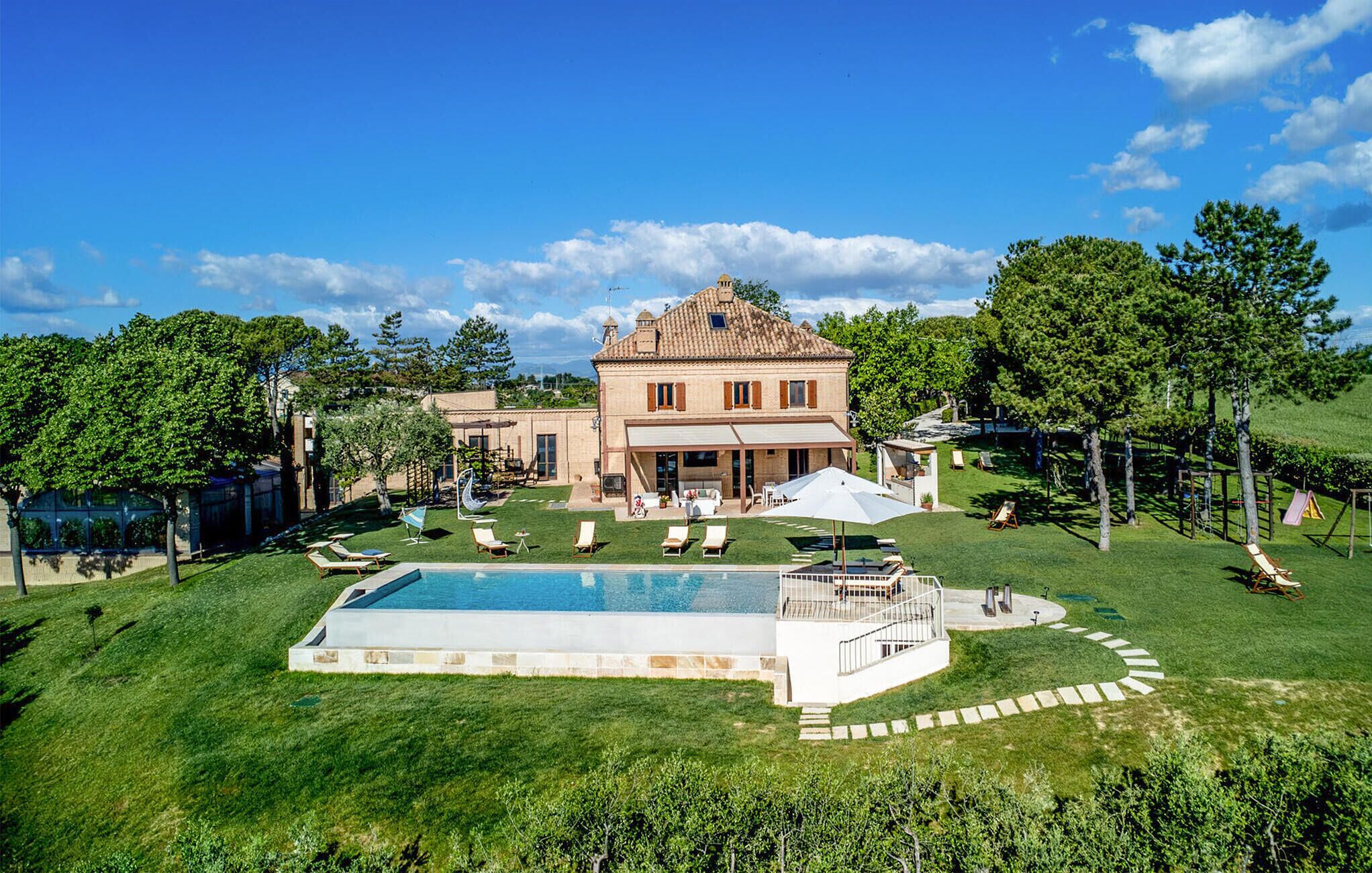 A large house with a swimming pool, a covered patio, and a well-maintained lawn.
