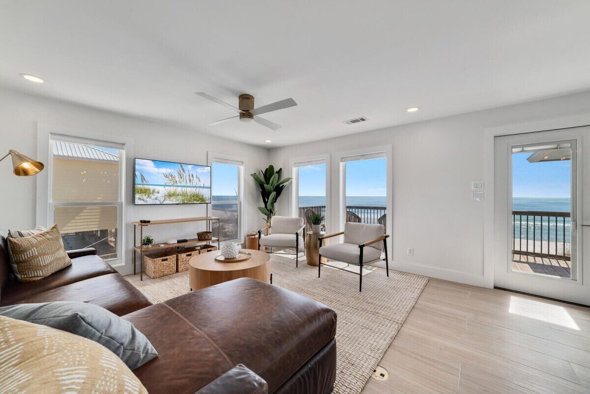 A spacious living room with a large window overlooking the ocean, a ceiling fan, and a cozy seating area with a leather couch and armchairs.