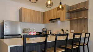 Egy modern konyha, melyben fa borítású szekrények, rozsdamentes acél hűtőszekrény, kávéfőző és bárszékek találhatók.