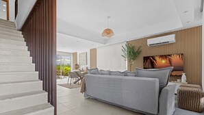 Una sala de estar moderna con un sofá gris, una escalera y un televisor de pantalla plana en la pared.